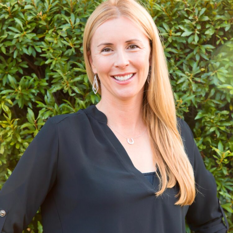 A woman standing in front of bushes smiling for the camera.