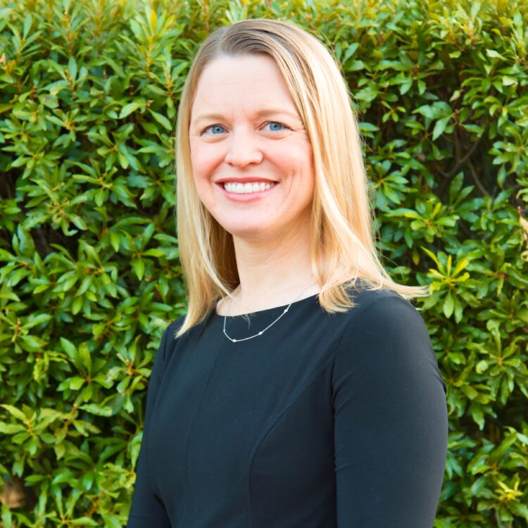 A woman standing in front of a bush smiling.