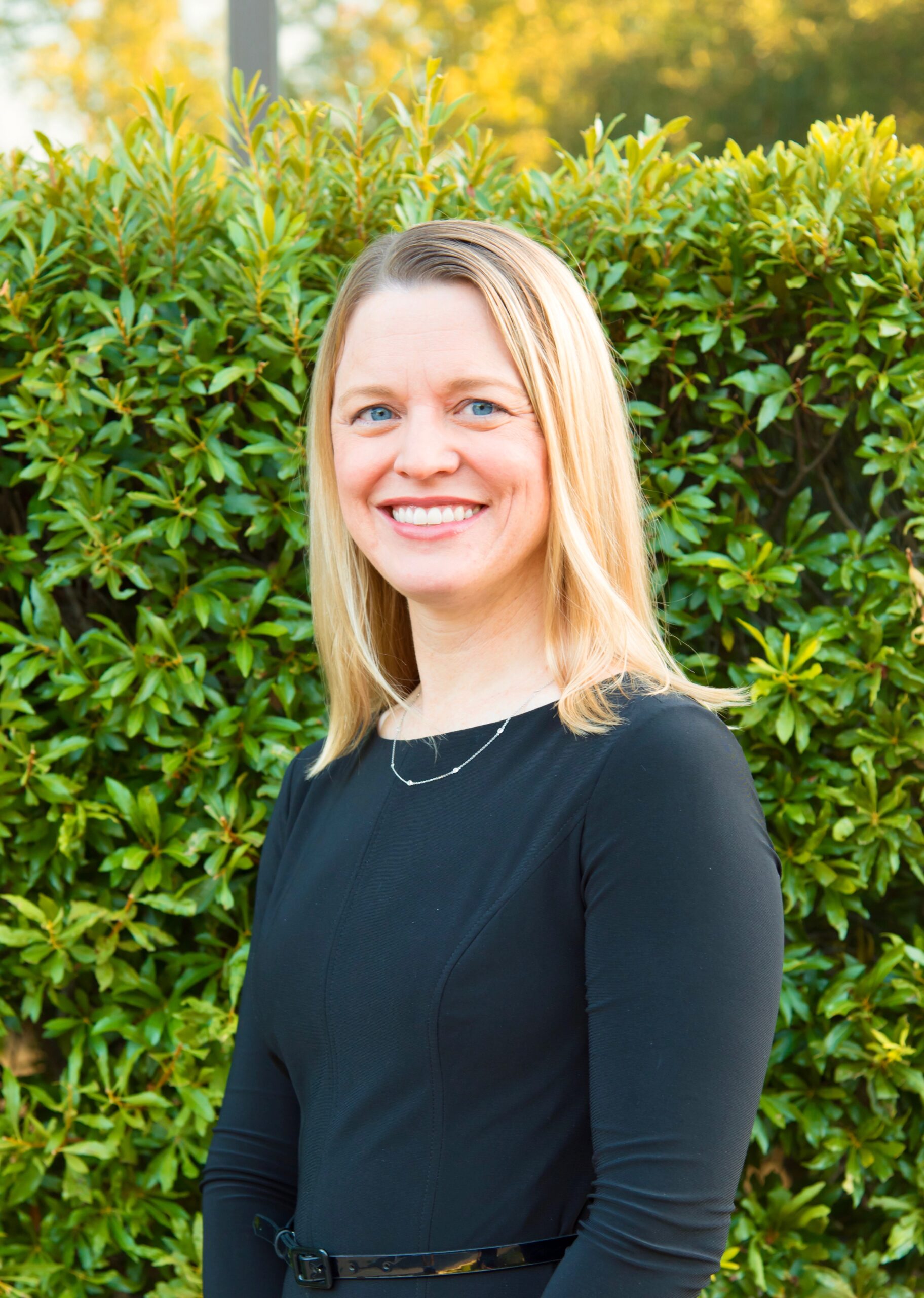 A woman standing in front of a bush smiling.