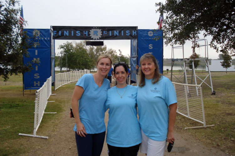 Three women standing in front of a blue sign.