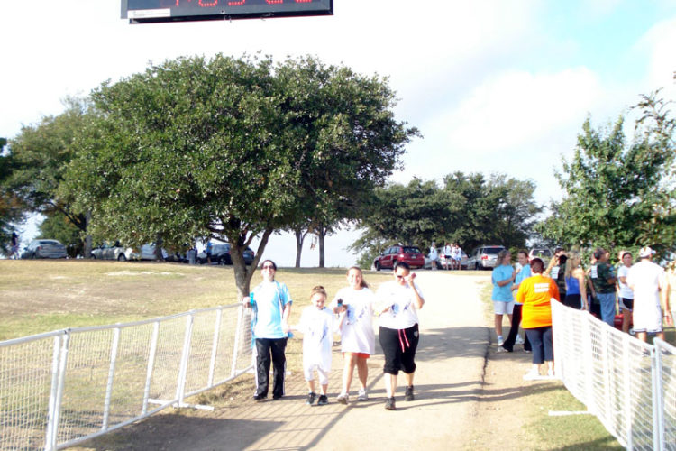 A group of people walking on the sidewalk near a fence.