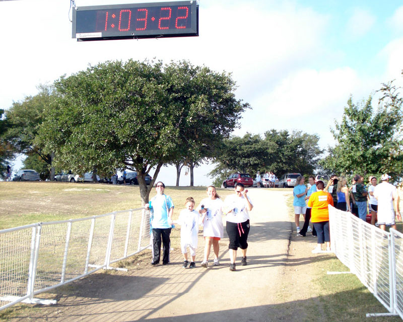 A group of people walking on the sidewalk near a fence.