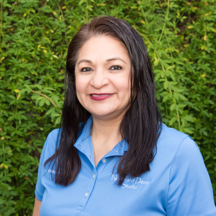 A woman in blue shirt standing next to green bushes.
