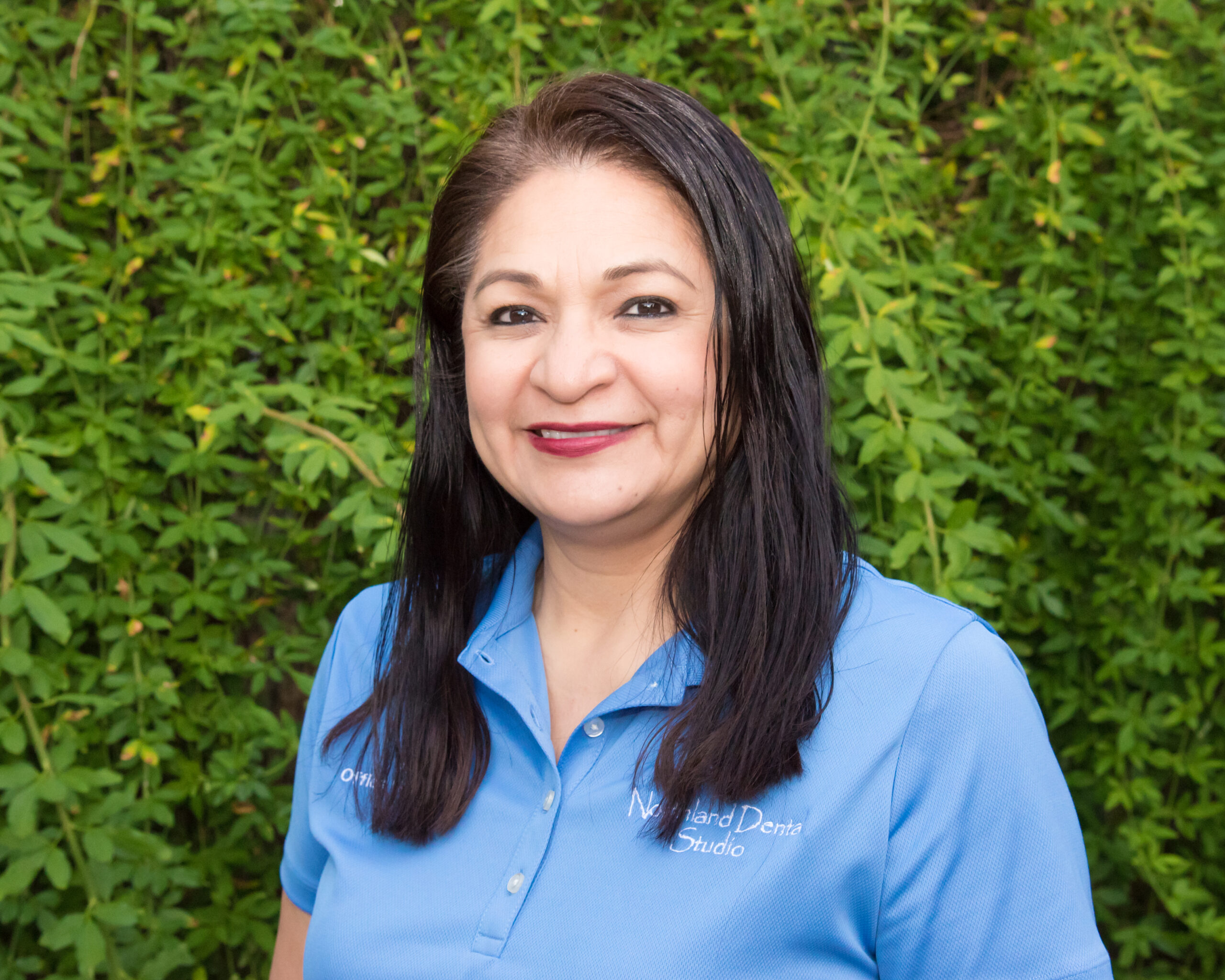 A woman in blue shirt standing next to green bushes.