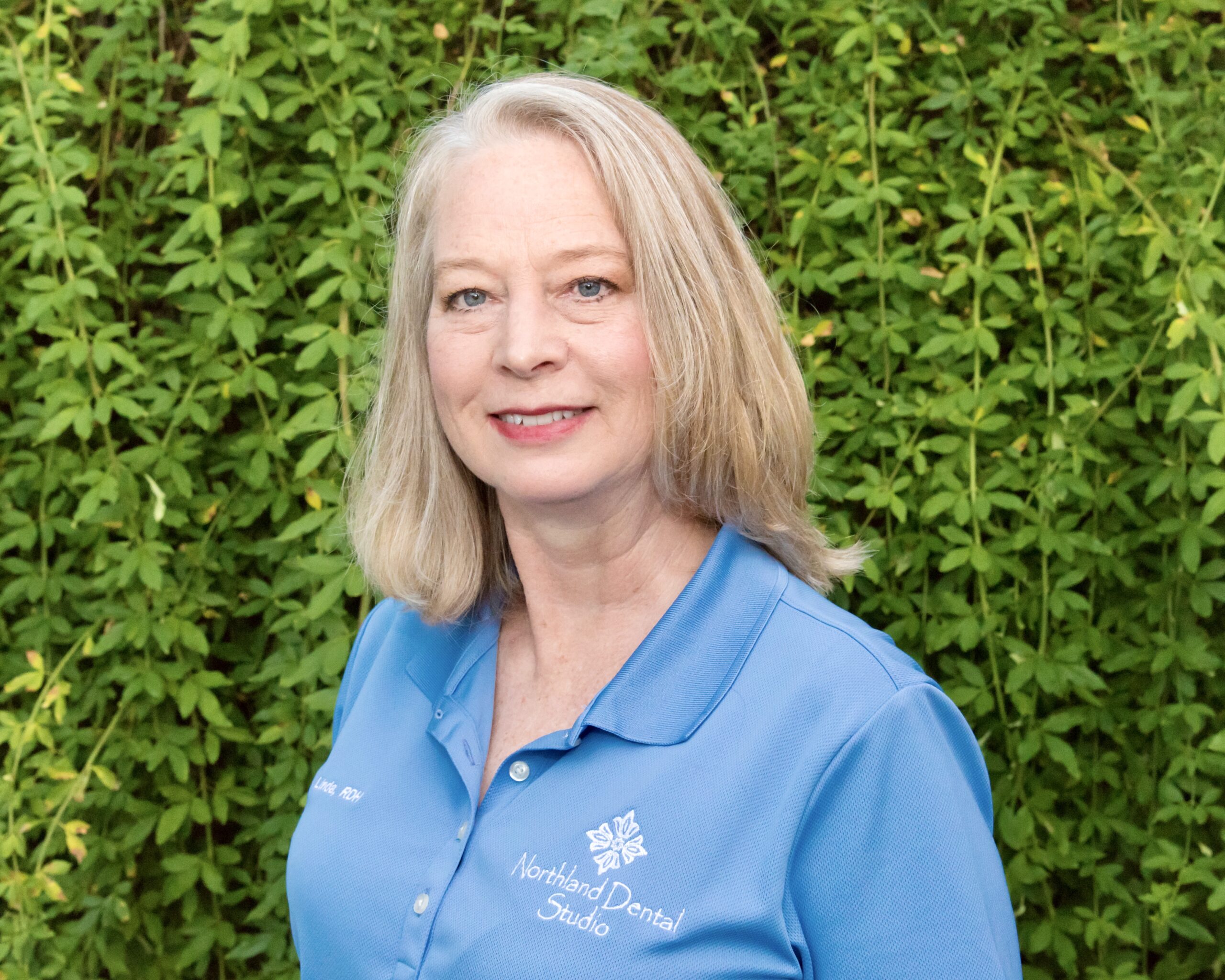 A woman standing in front of a wall with green plants.