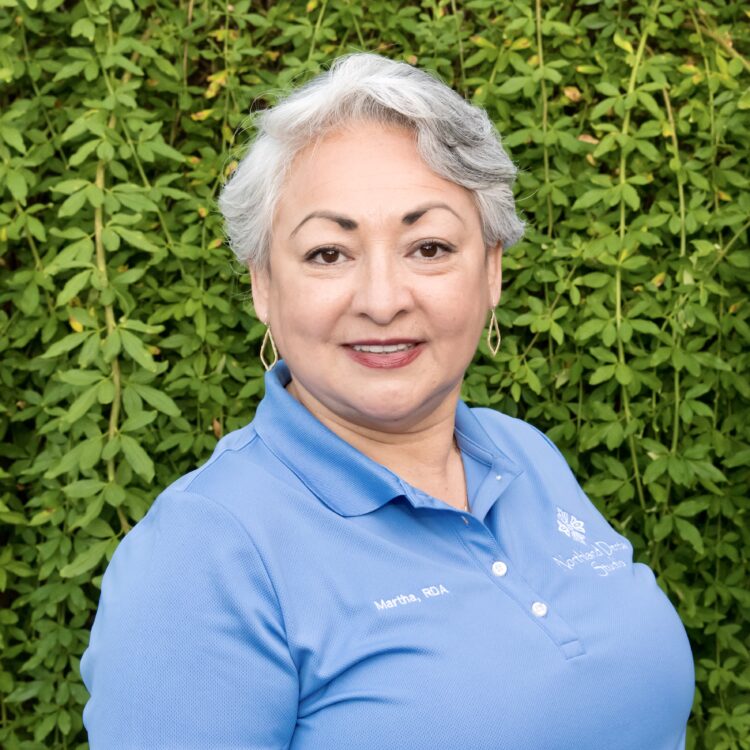 A woman standing in front of a wall with bushes.