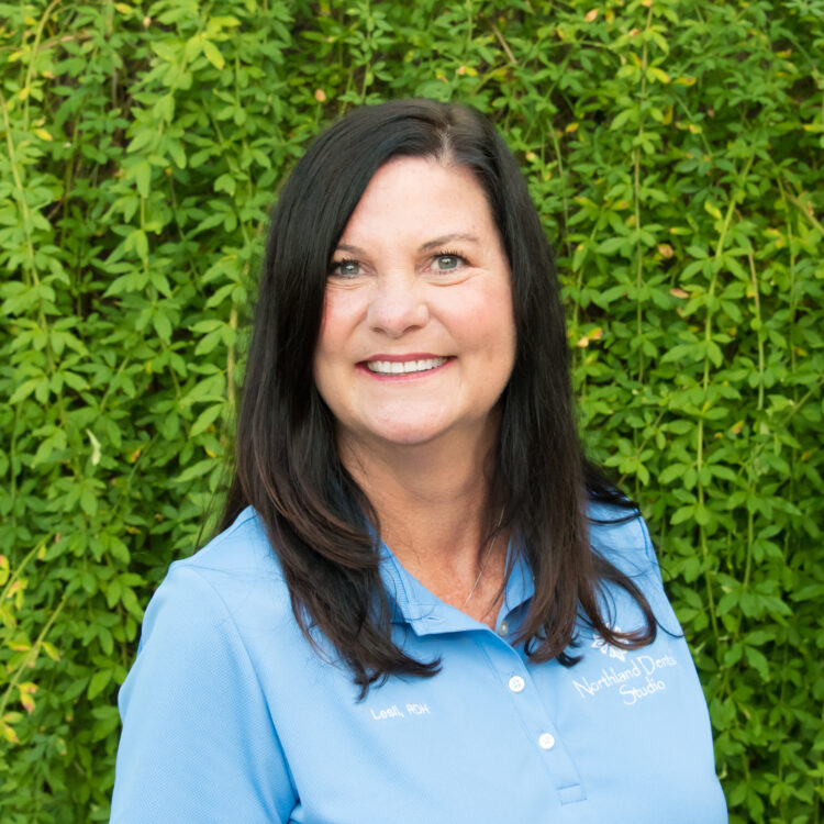 A woman standing in front of a wall with green bushes.