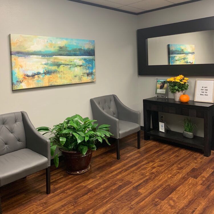 A room with two gray chairs and a painting on the wall.