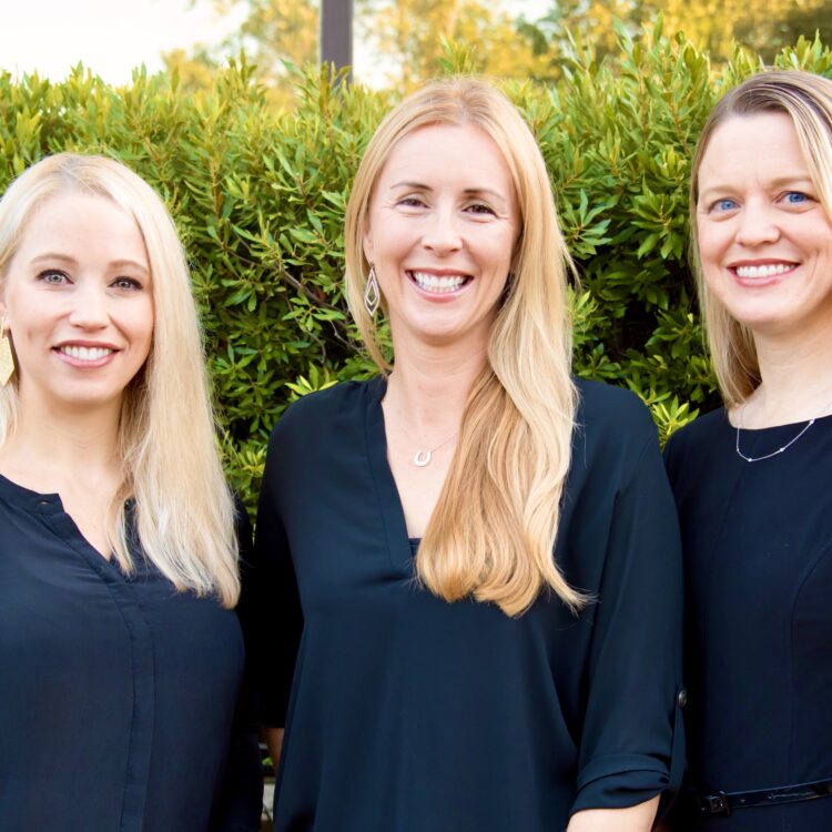 Three women standing next to each other in front of a bush.